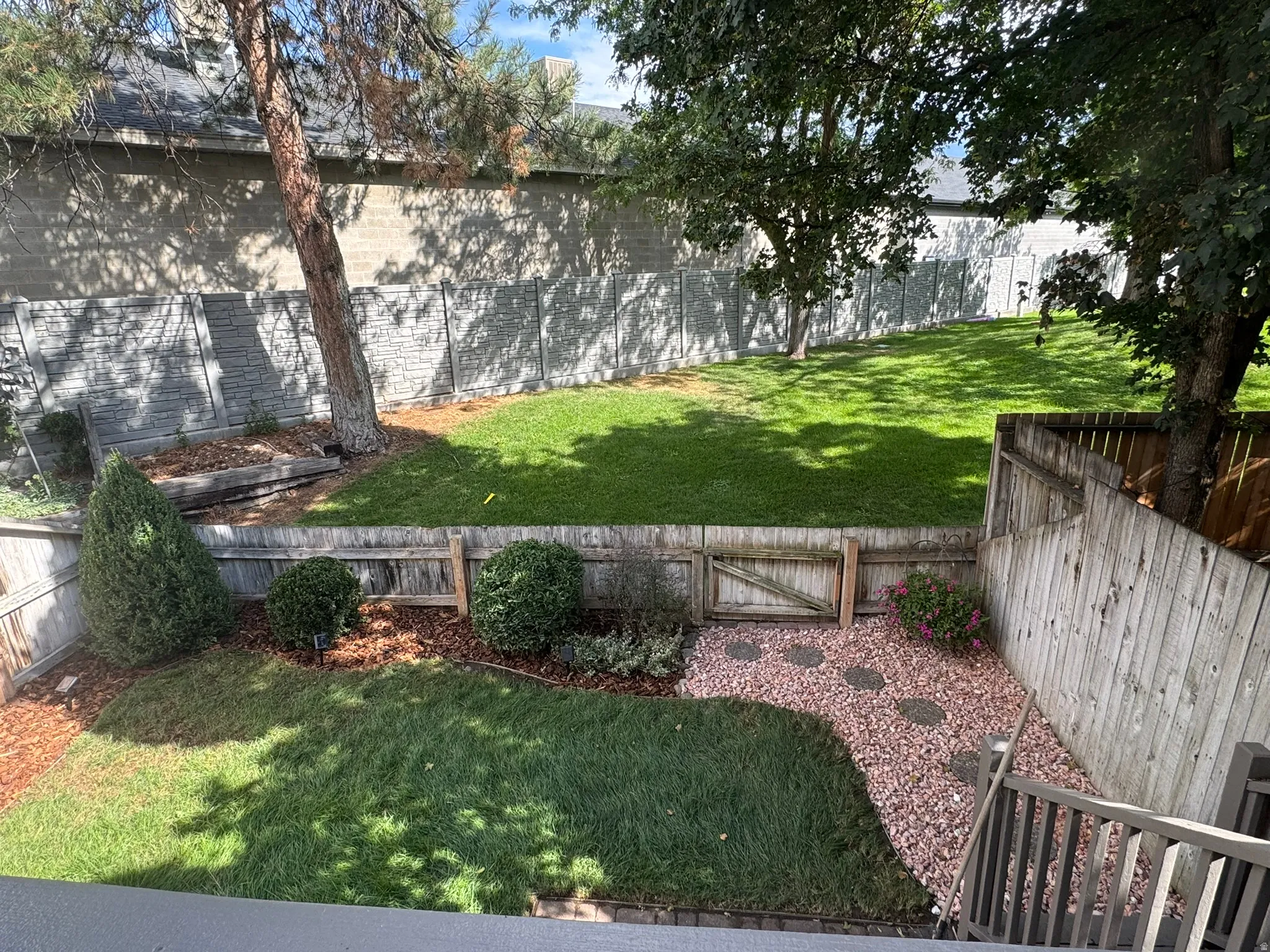 Backyard featuring a manicured lawn, established trees, wood fencing, and a decorative gravel pathway with stepping stones