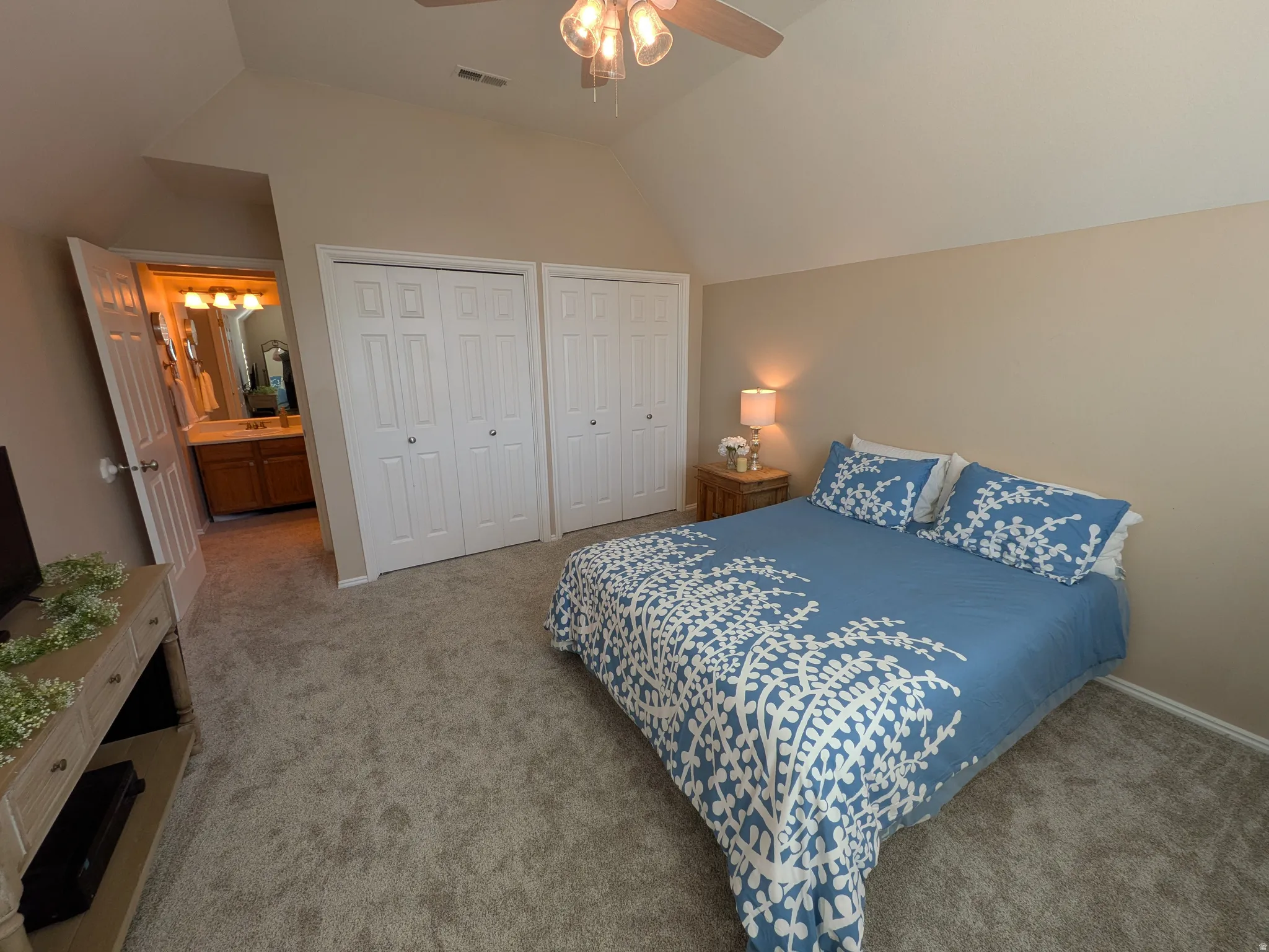 Vaulted ceiling with a ceiling fan, two bi-fold door closets, and carpet flooring