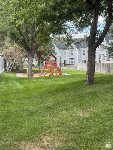 Landscaped common area featuring mature trees, a wooden play structure, and green lawn space