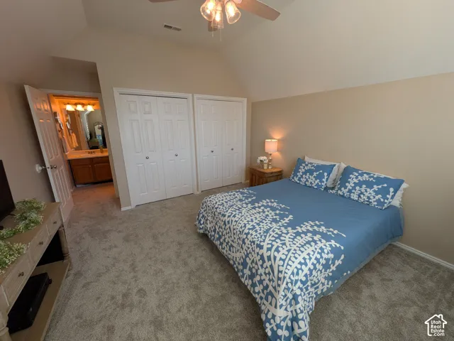 Vaulted ceiling with a ceiling fan, two bi-fold door closets, and carpet flooring