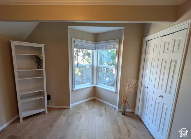 Wood-finish flooring, corner bay window, crown molding, and bifold closet doors