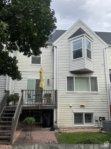 Rear exterior featuring a multi-level deck with stairs, a brick patio, and a grass area