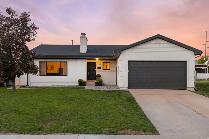 Single-story residence featuring a dark asphalt shingle roof, white stucco exterior, and a two-car garage with a dark panel door