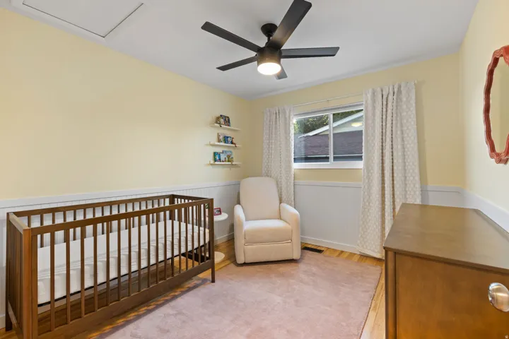 Wood-finish flooring, white paneled wainscoting, and a ceiling fan with integrated lighting