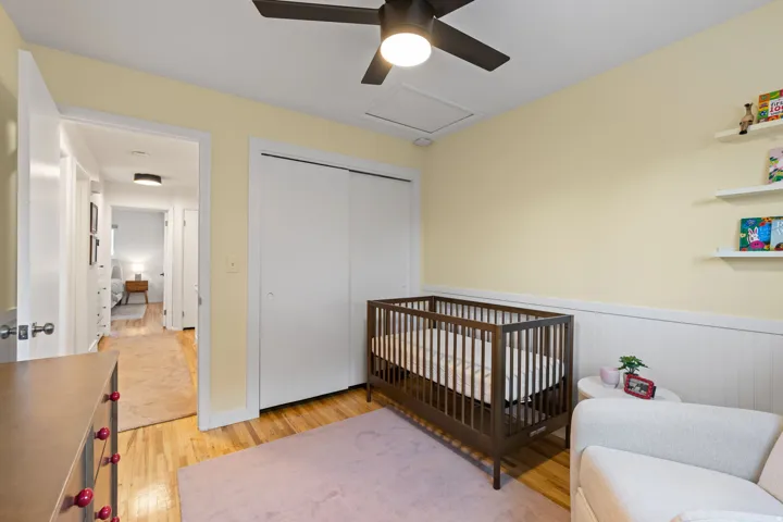 Hardwood flooring, ceiling fan with integrated lighting, built-in shelving, white paneled wainscoting, and white sliding closet doors