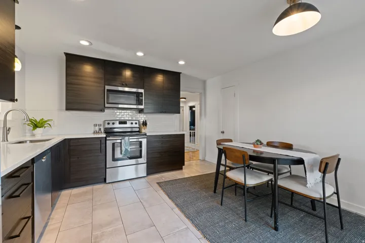 Kitchen featuring dark wood-finish cabinetry, stainless steel appliances, white subway tile backsplash, and light-toned tile flooring
