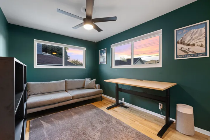 Wood-finish flooring with a ceiling fan, deep green walls, and large windows