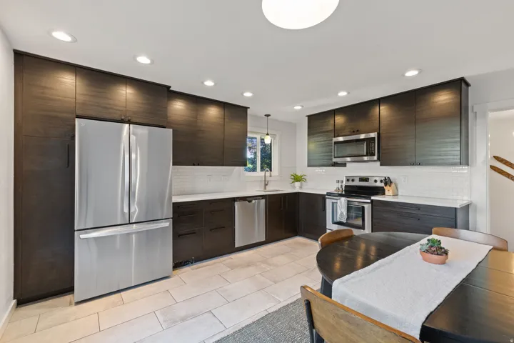 Sleek kitchen featuring dark wood-finish cabinetry, stainless steel appliances, light-toned countertops, white subway tile backsplash, and recessed lighting