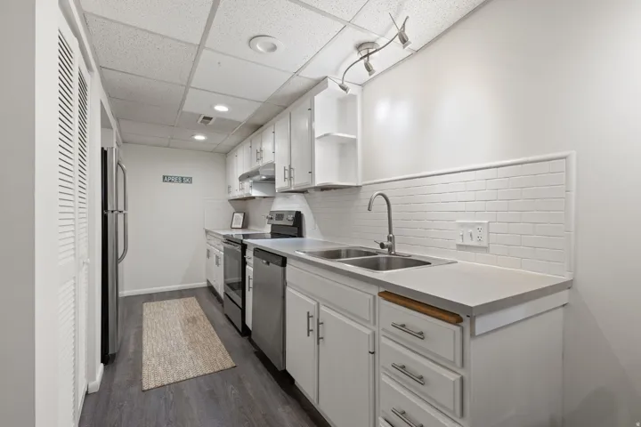 Kitchen featuring white cabinetry, stainless steel appliances, white subway tile backsplash, and wood-finish flooring