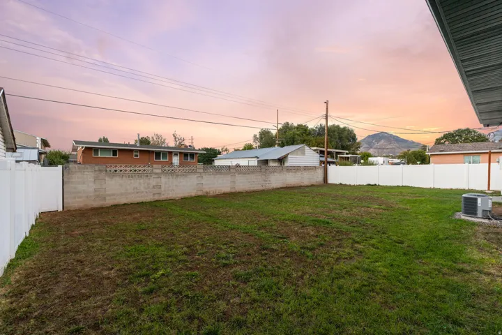 Expansive backyard featuring a manicured lawn, a concrete block wall, and white vinyl fencing