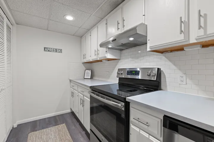 White cabinetry with brushed nickel hardware, white subway tile backsplash, stainless steel appliances, and wood-finish flooring