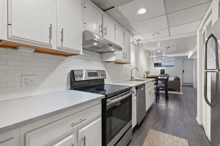 Kitchen with white cabinetry, subway tile backsplash, stainless steel appliances, and wood-finish flooring