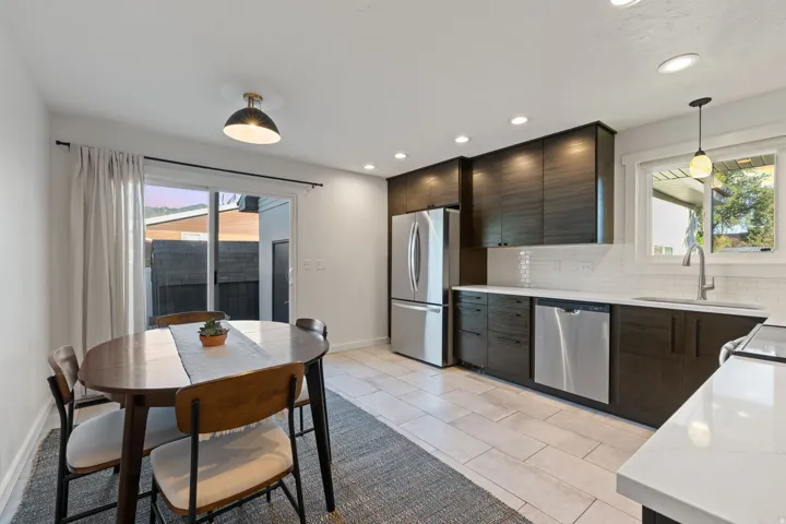 Modern kitchen with dark wood-finish cabinetry, white subway tile backsplash, stainless steel appliances, and light-colored tile flooring