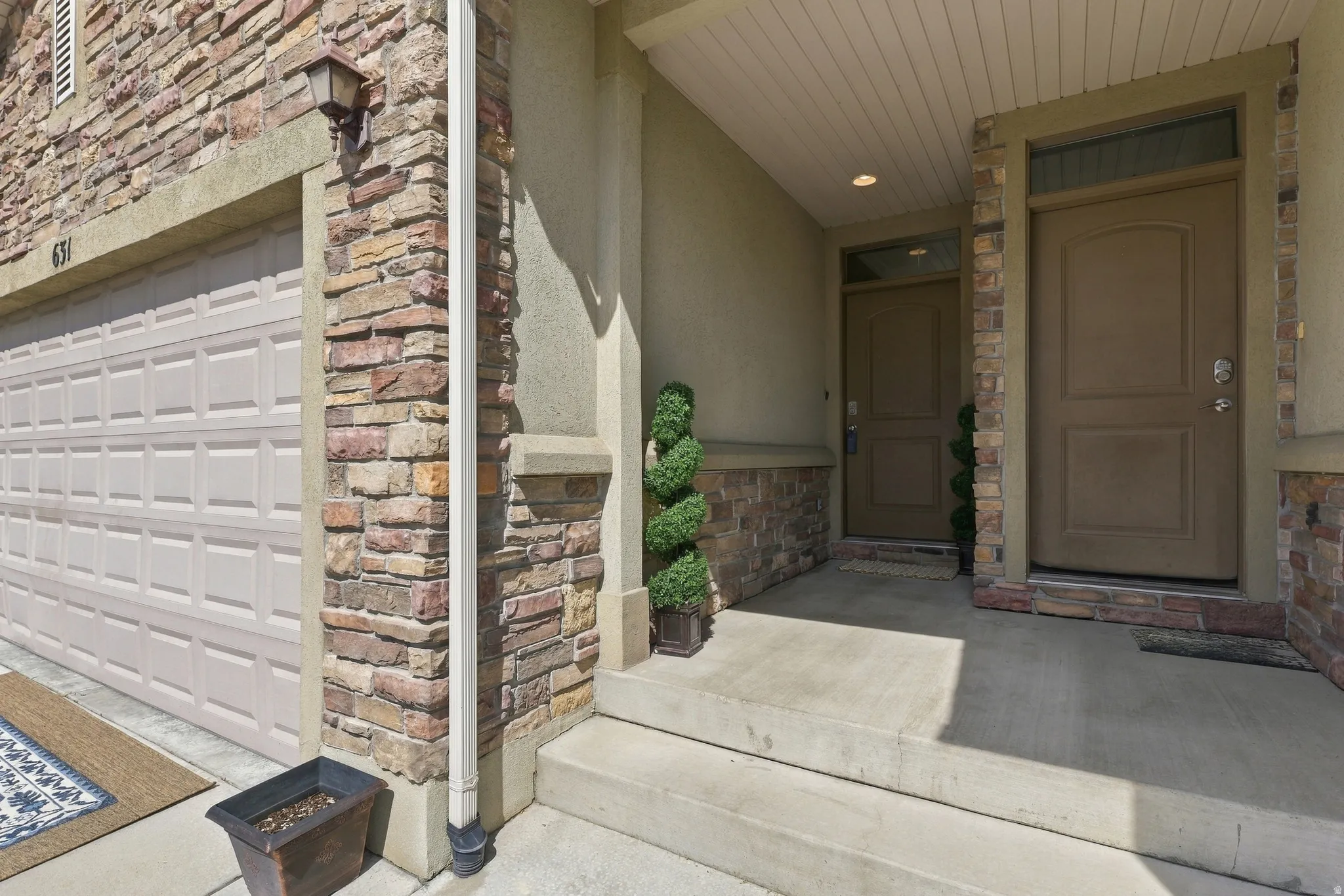 Stone veneer facade with stucco accents, an integrated garage door, covered entryway, and concrete steps