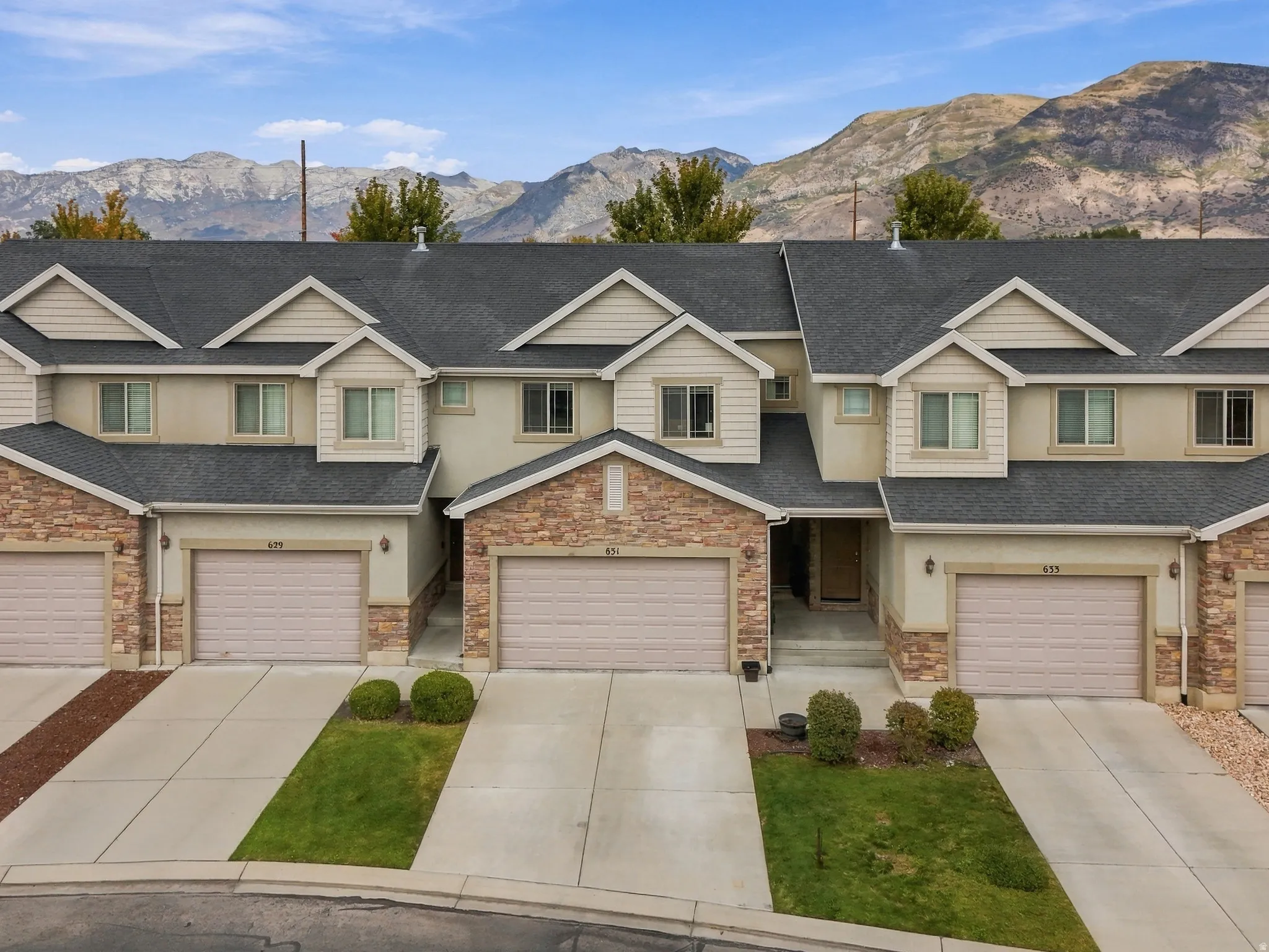 Front exterior featuring stone accents, stucco siding, multiple dormers, attached garages, and a paved driveway