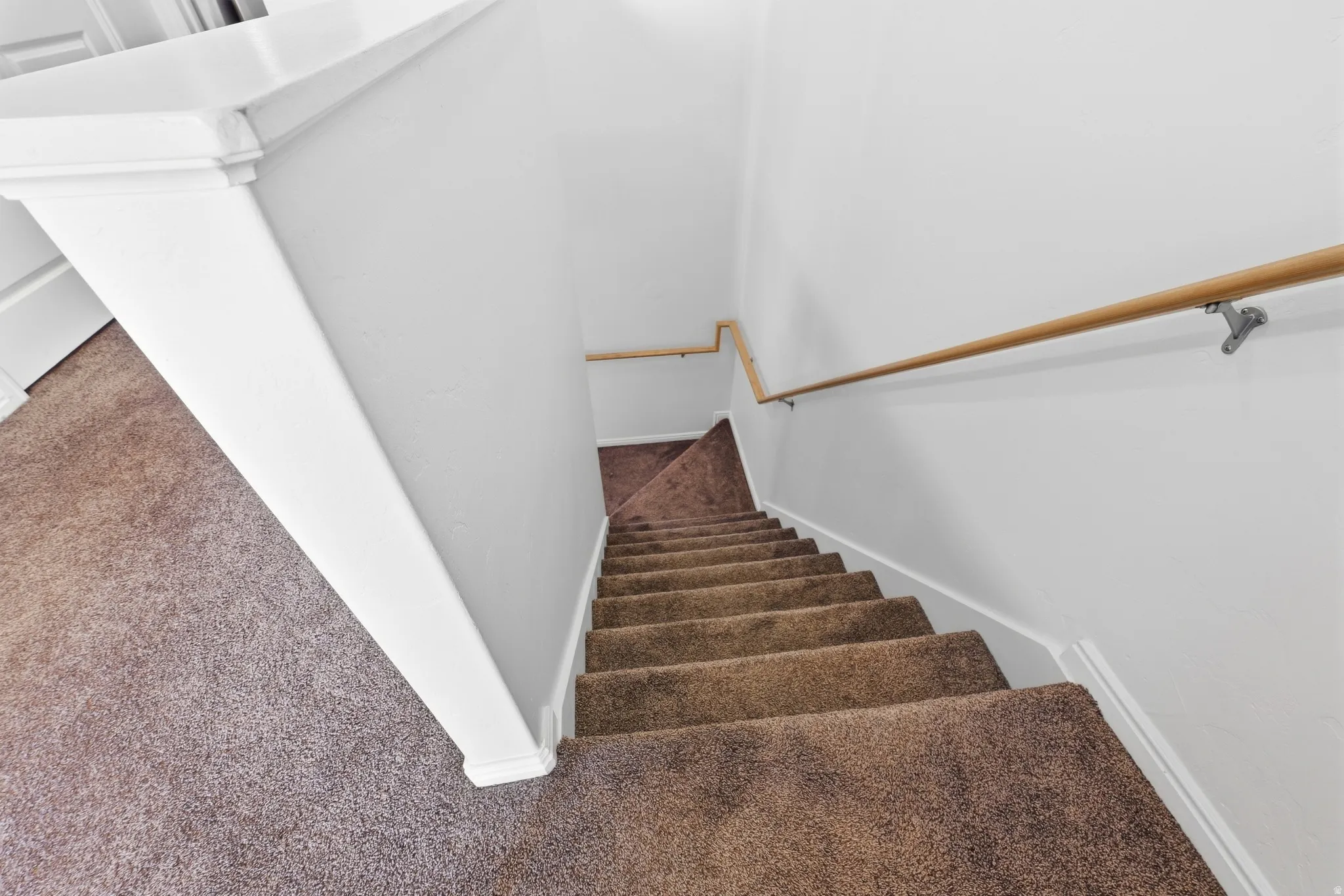 Carpeted staircase featuring a light wood-finish handrail and white painted walls