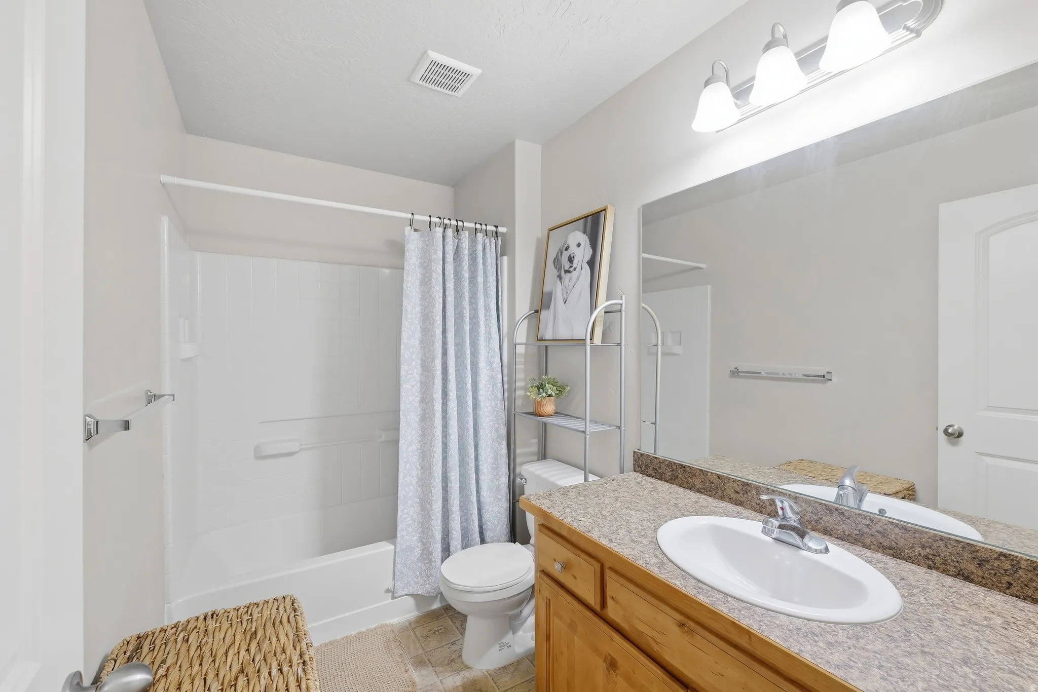 Integrated bathtub and shower combination, wood-finish vanity with an oval basin, speckled countertop, and a mirrored wall