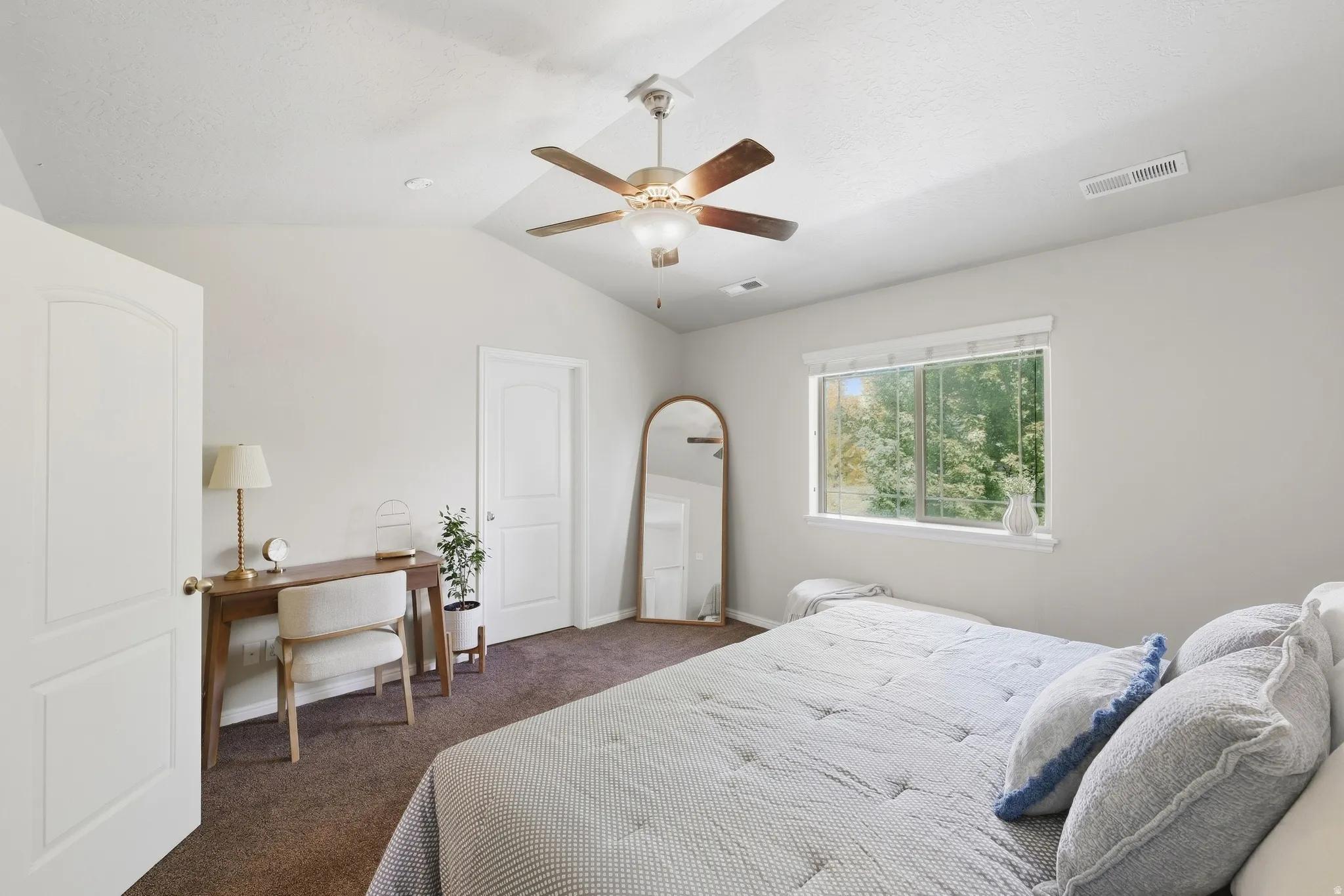 Vaulted ceiling with ceiling fan, arched panel door, large window with roller shade, and neutral wall paint
