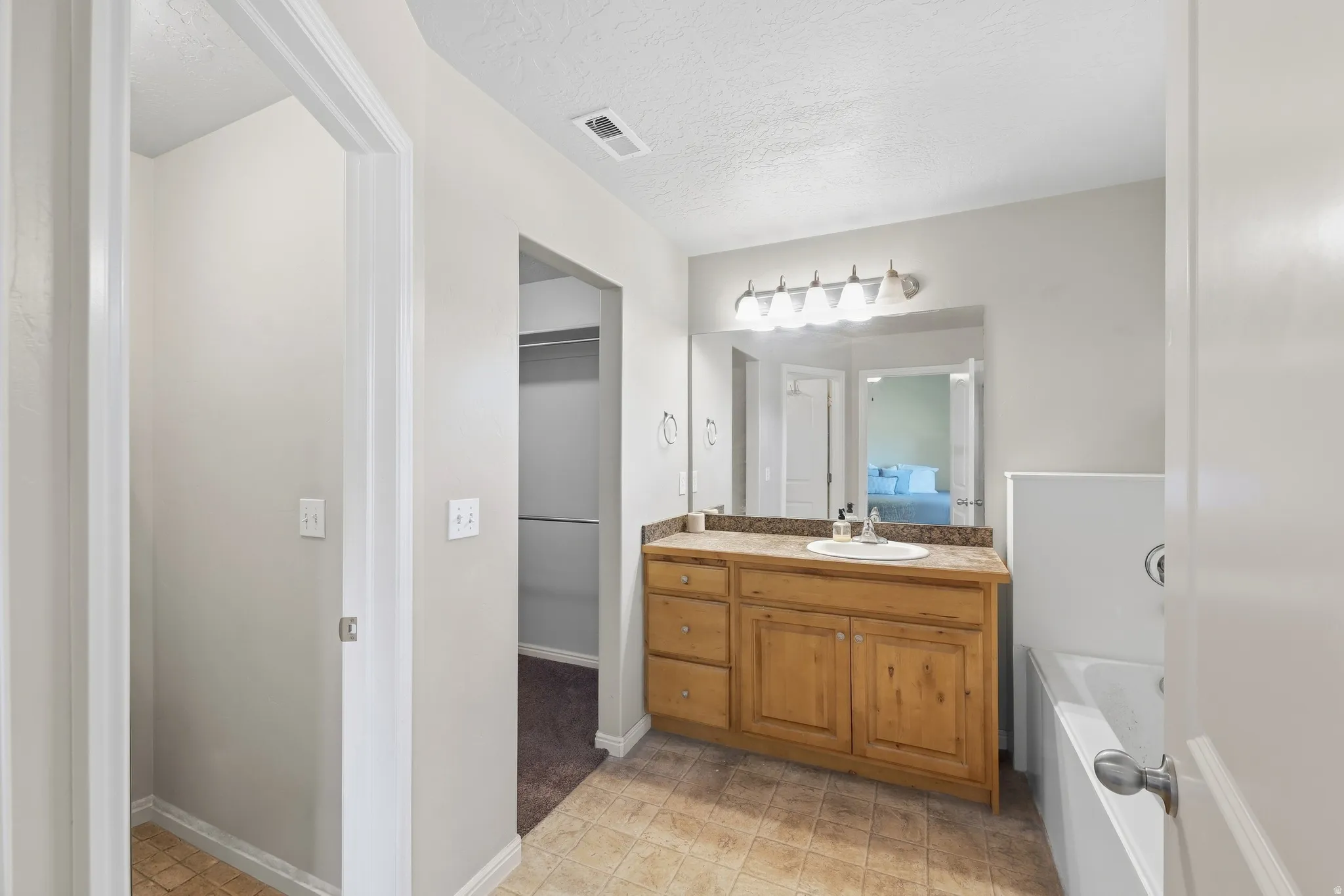 Bathroom featuring a single vanity with wood cabinetry, a built-in bathtub, and tile flooring