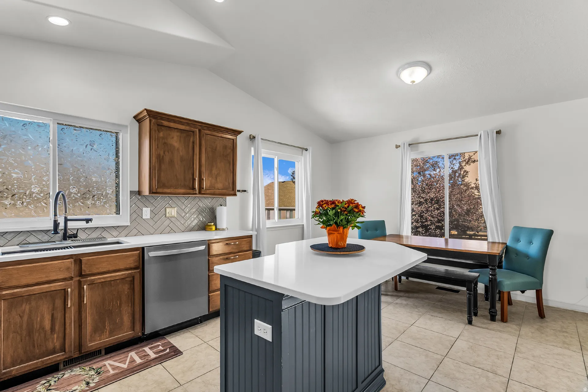 Kitchen featuring a vaulted ceiling with recessed lighting, central island with quartz countertops, new stainless steel appliances and an upgrades herringbone pattern tile backsplash.
