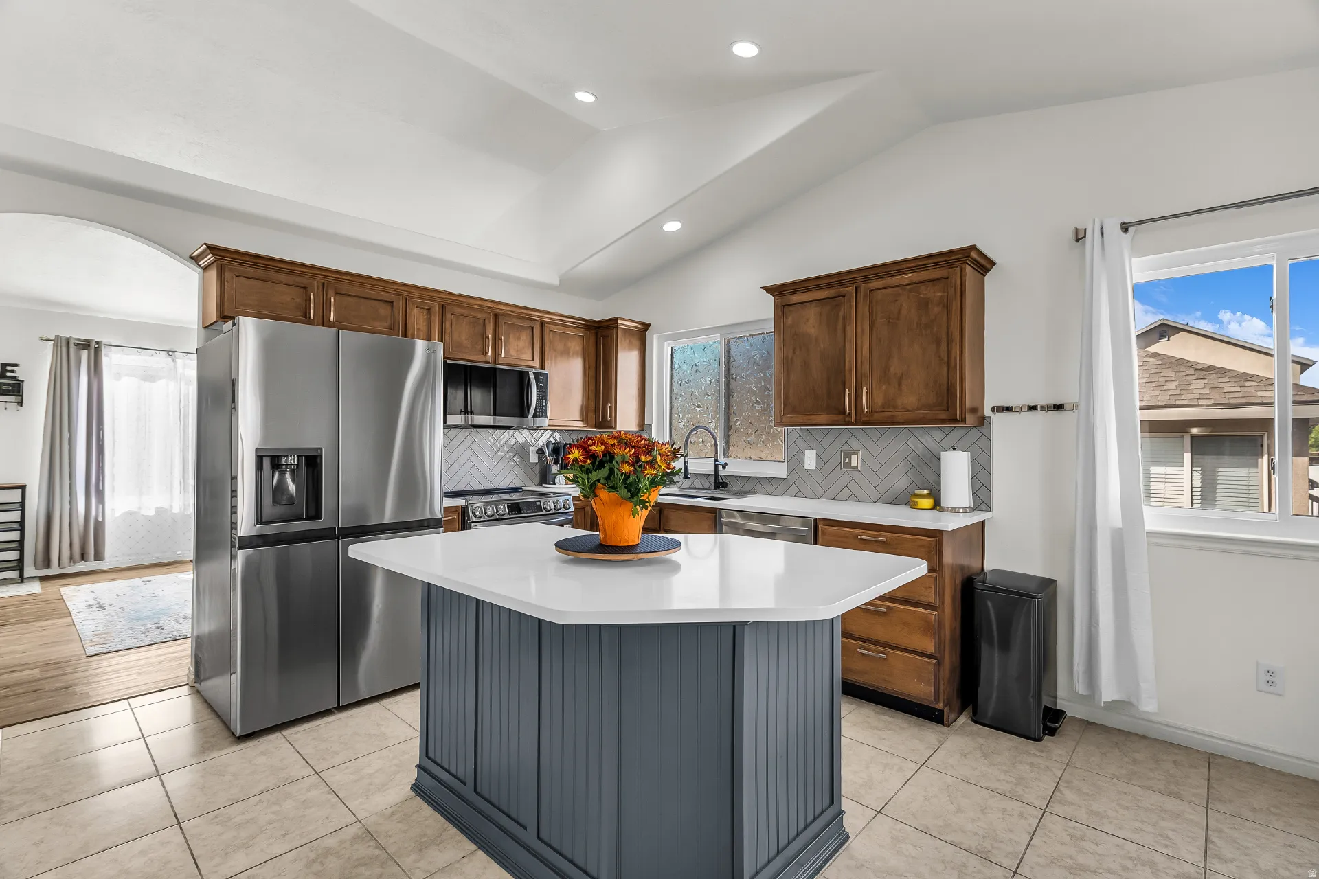 Kitchen featuring a central island with quartz countertops, new stainless steel appliances and an upgraded herringbone pattern tile backsplash.