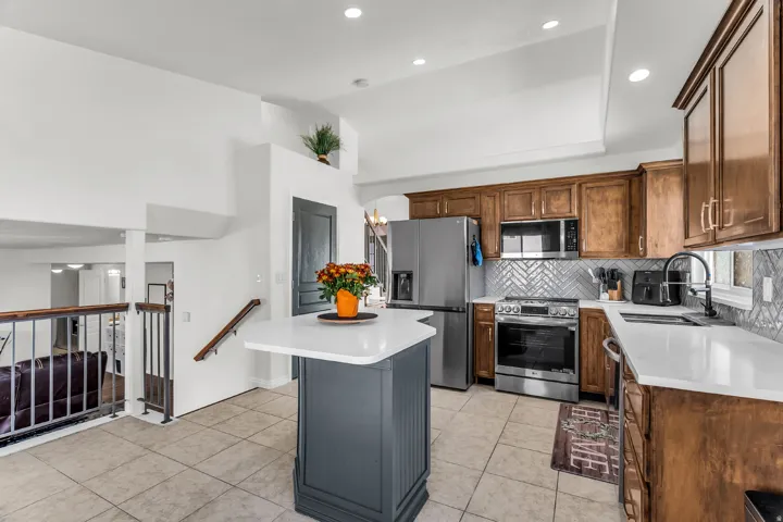 Kitchen featuring new stainless steel appliances, quartz countertops, upgraded herringbone tiled backsplash, vaulted ceilings with recessing lighting.