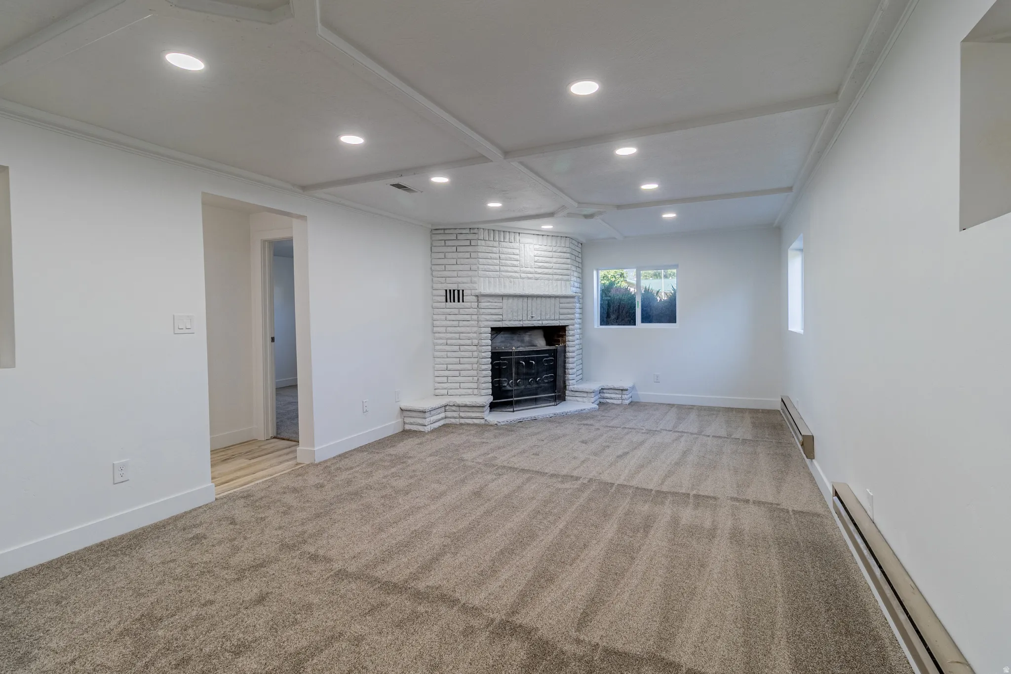 Recessed lighting illuminates a coffered ceiling, complemented by a white brick fireplace with a decorative mantel and hearth