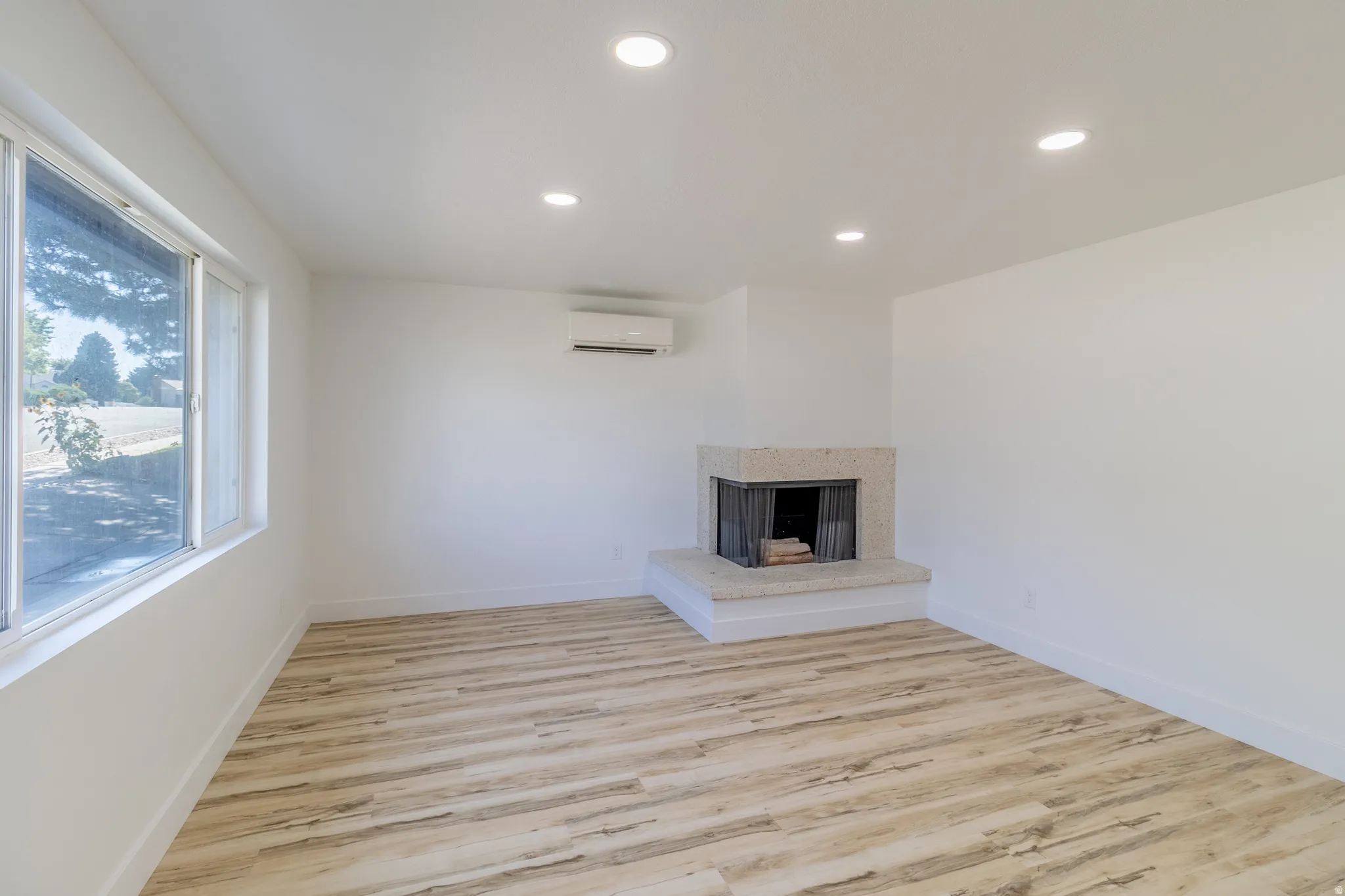Recessed lighting, wood-finish flooring, a contemporary fireplace with a stone hearth, and a ductless mini-split system