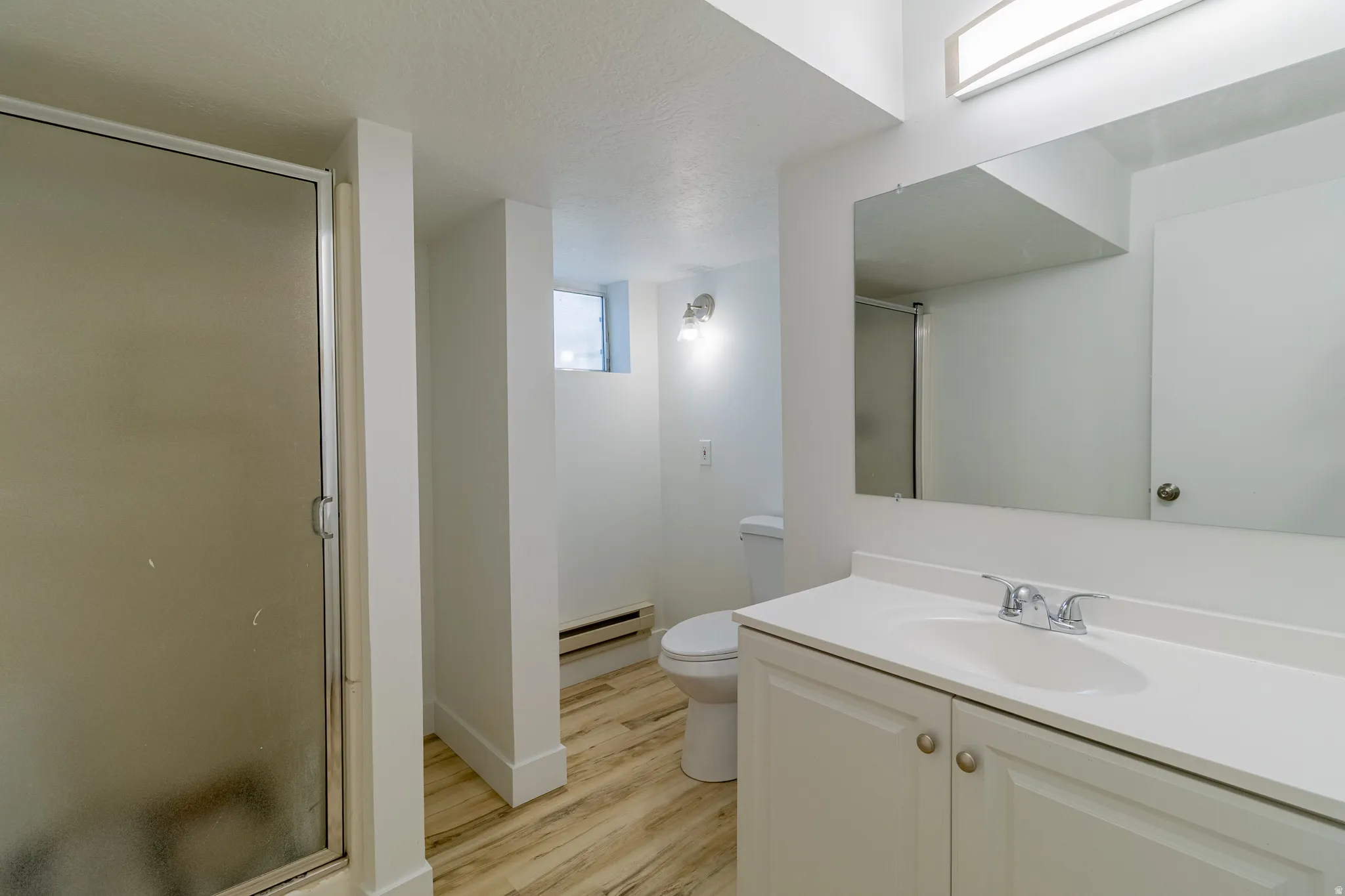 Bathroom featuring a shower with a frosted glass enclosure, a vanity with a white countertop and integrated sink, a large wall-mounted mirror, and wood-finish flooring