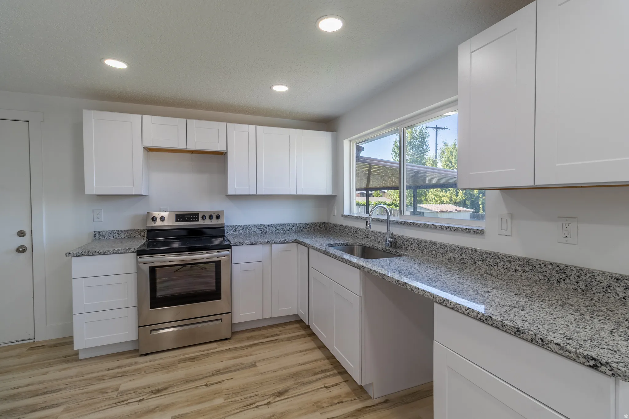 Kitchen featuring white cabinetry, wood-finish flooring, stainless steel range, granite-style countertops, and a stainless steel sink with a high-arc faucet