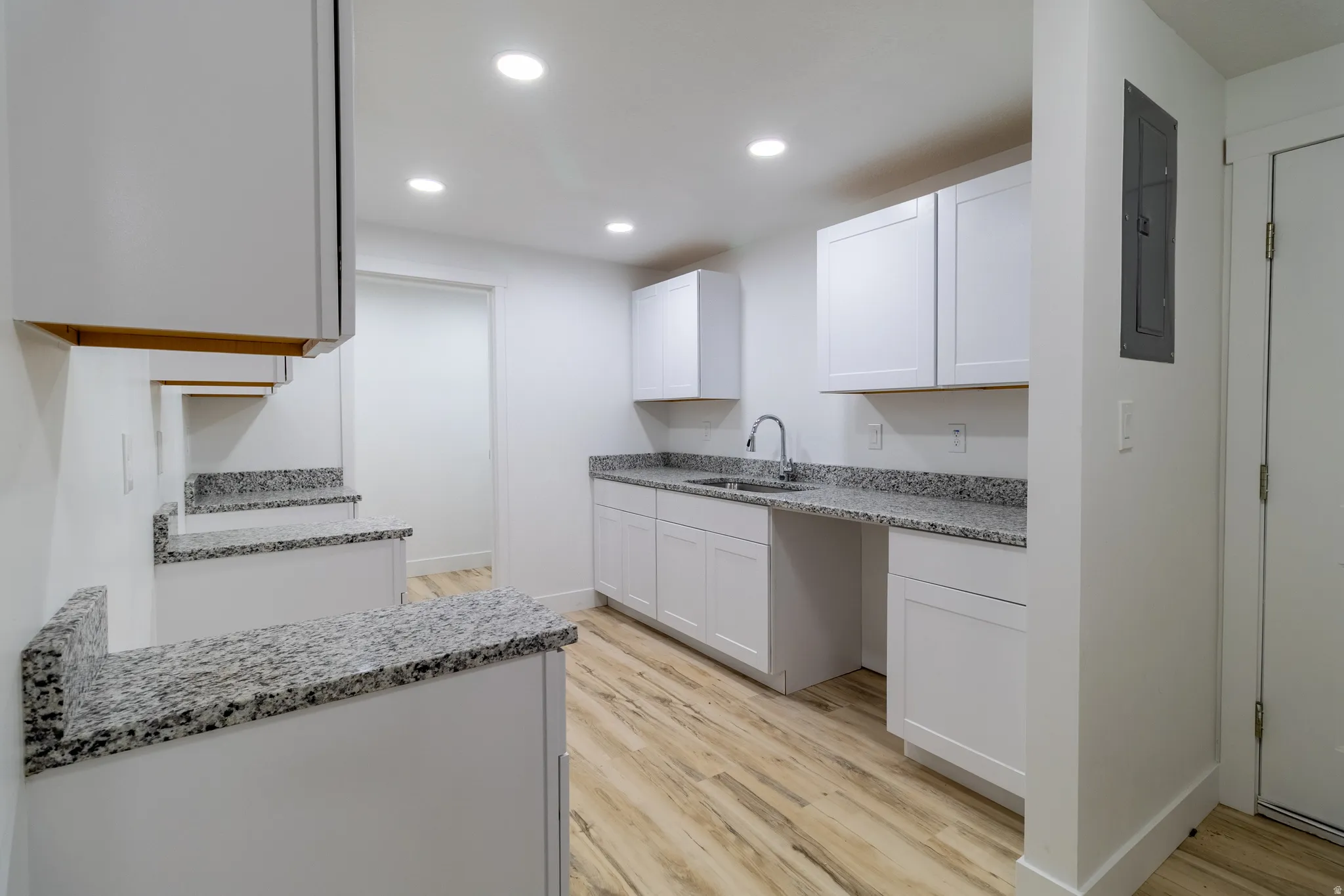 Recessed lighting illuminates the white cabinetry and light-toned wood-finish flooring