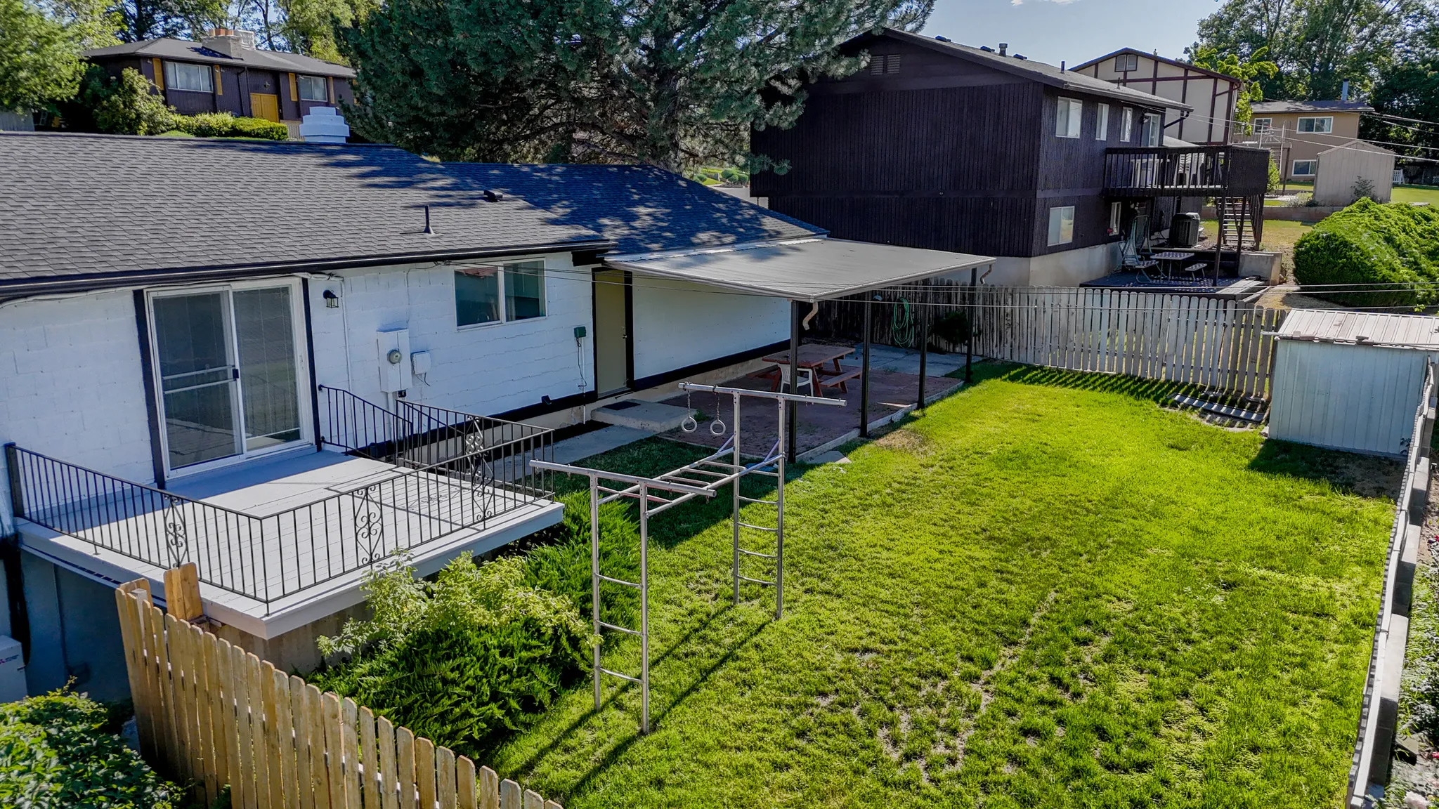 Expansive backyard featuring a manicured lawn, a covered patio, and a deck with metal railings