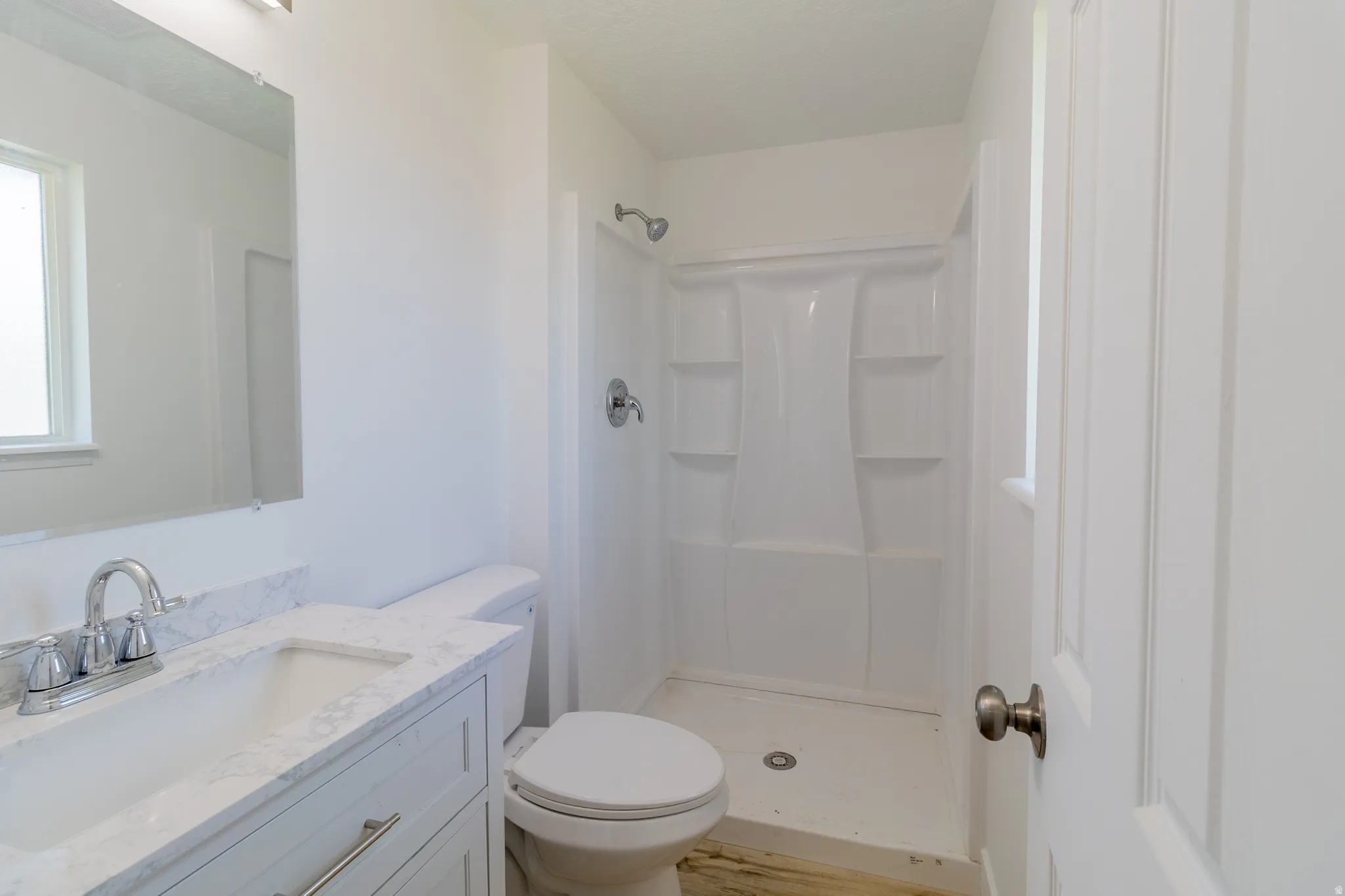 Vanity with integrated sink and chrome faucet, single toilet, and shower with white surround