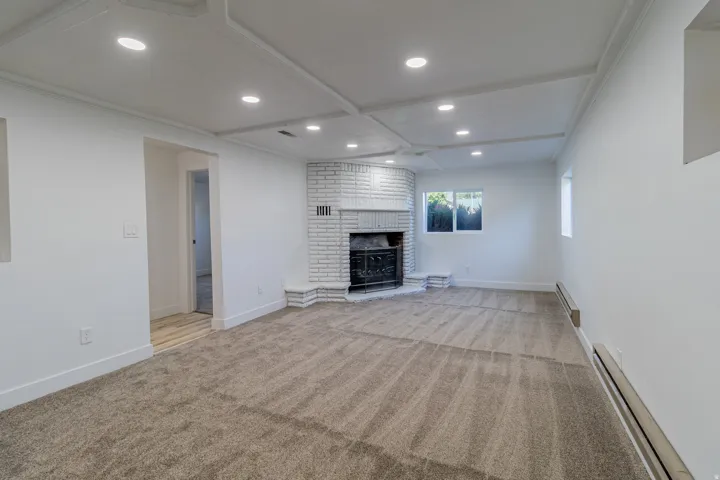 Recessed lighting illuminates a coffered ceiling, complemented by a white brick fireplace with a decorative mantel and hearth