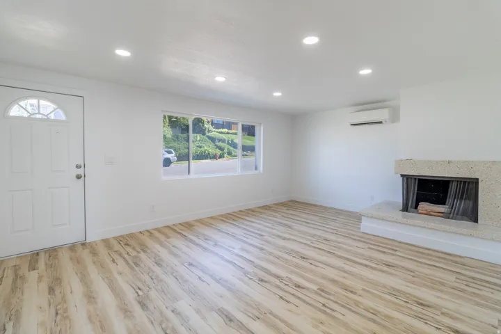 Recessed lighting, light wood-finish flooring, white walls, stone-clad fireplace, and wall-mounted climate control unit