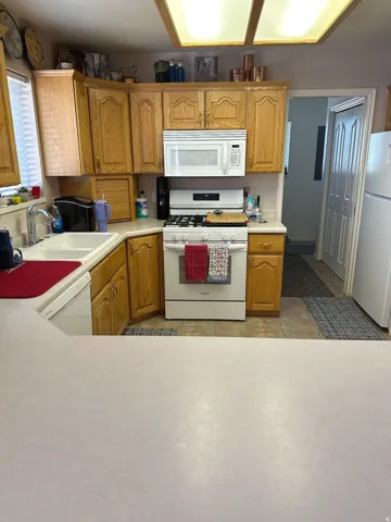 U-shaped kitchen featuring wood cabinetry, integrated microwave, gas range, and white appliances