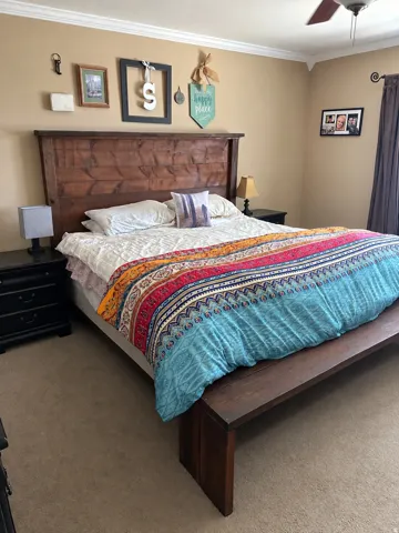 Wood-finish headboard, crown molding, ceiling fan, and carpet flooring