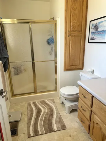 Shower with gold-toned framed enclosure, wood-finish cabinetry, and solid surface countertop