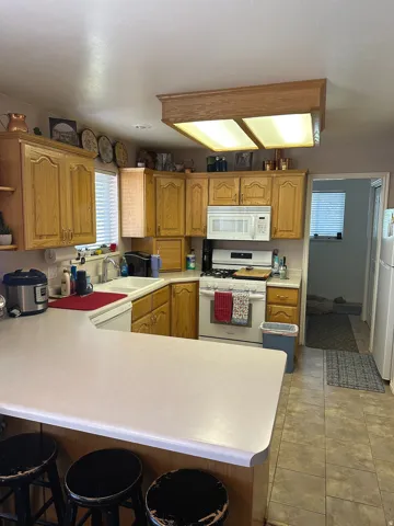 Kitchen featuring a U-shaped countertop, wood-finish cabinetry, built-in microwave, white kitchen appliances, and tiled flooring