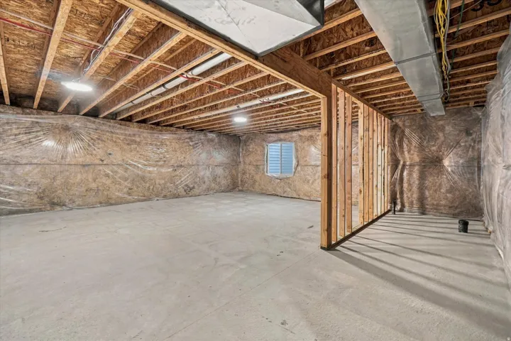 Unfinished basement featuring concrete flooring, exposed ceiling joists, framed partition walls, and a window with horizontal blinds