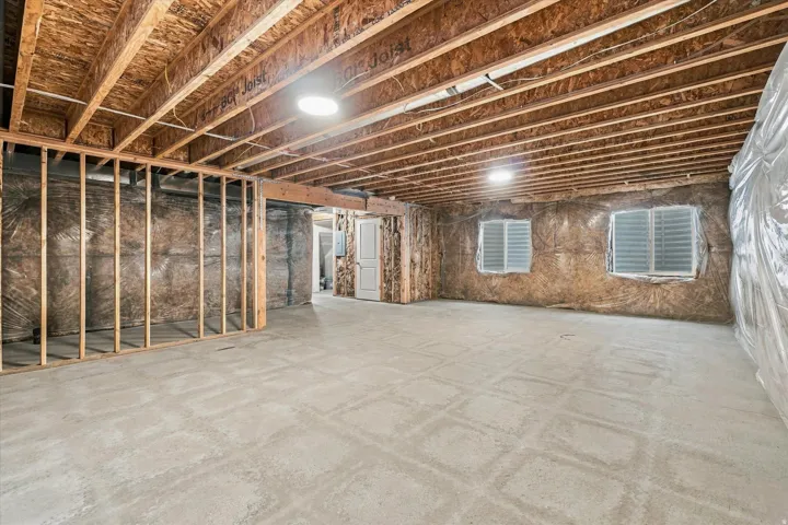 Unfinished basement with exposed ceiling joists, concrete flooring, interior framing, and two windows