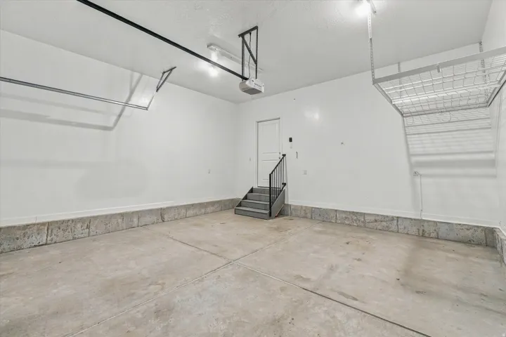 Concrete flooring, interior stairs with railing, overhead storage rack, overhead garage door track system, and wall-mounted lighting