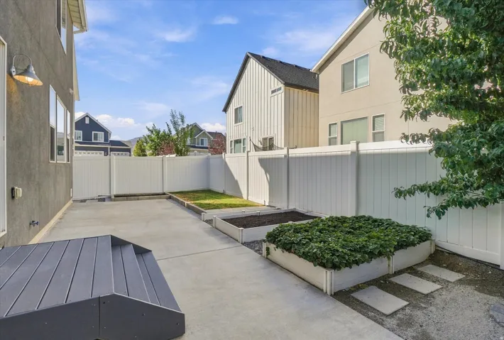 Concrete patio with a composite staircase, white panel fencing, and raised garden beds