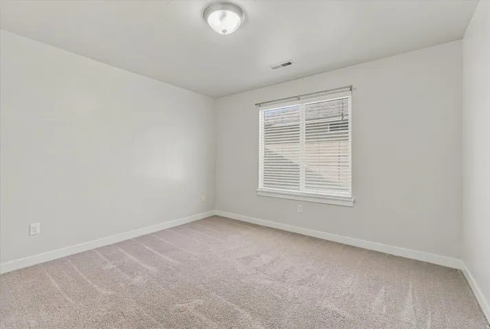 Neutral carpet flooring, white walls, flush mount ceiling light, and a window with blinds