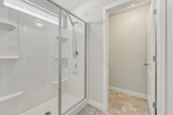 Shower enclosure with clear glass door, integrated shelving, and a ceiling-mounted light fixture