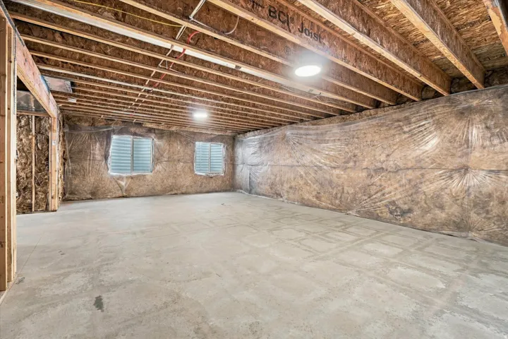 Unfinished basement featuring exposed wood joists, concrete flooring, two windows, and built-in lighting