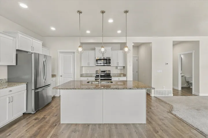 Kitchen featuring an island with a sink, white cabinetry, integrated stainless steel appliances, granite countertops, and wood-finish flooring