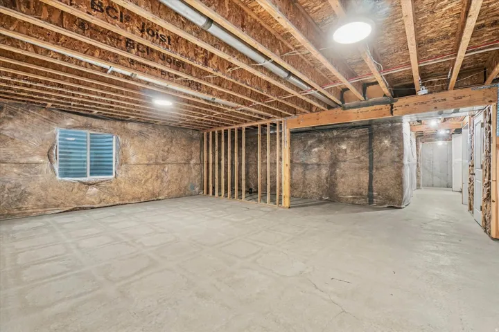Unfinished basement featuring exposed wood joists, concrete flooring, and a small window