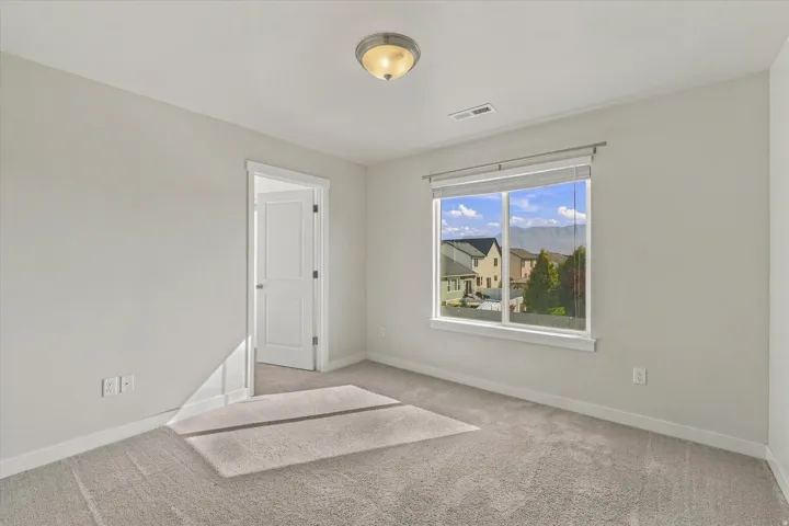 Expansive window, neutral wall paint, carpet flooring, ceiling-mounted light fixture, and a paneled door