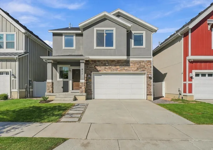 Stucco and stone facade with a two-car garage, concrete driveway, and front lawn